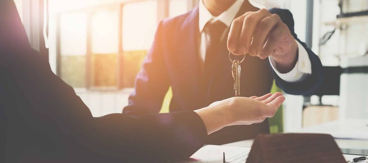 man in suit hands over keys to person with open palm