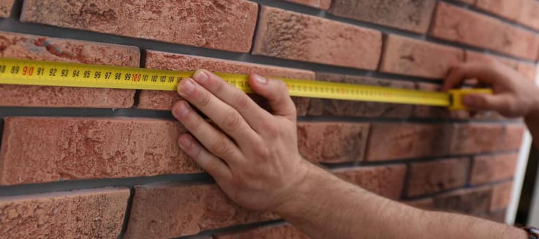 Man measuring brick wall, closeup. Construction tool