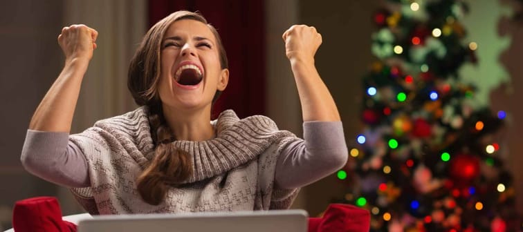 Happy woman with laptop rejoicing success in front of Christmas tree