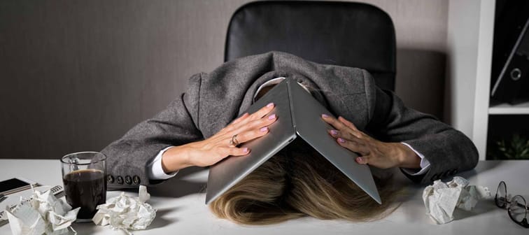Frustrated woman hiding under laptop in office