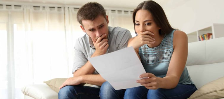Couple looking concerned, sitting on a couch with their hands over their mouths