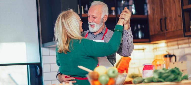 Beautiful senior couple is dancing and smiling while cooking together in kitchen