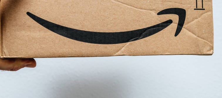 PARIS, FRANCE - JAN 6, 2018: Hand holding cardboard box with Amazon Logotype Smile logo arrow