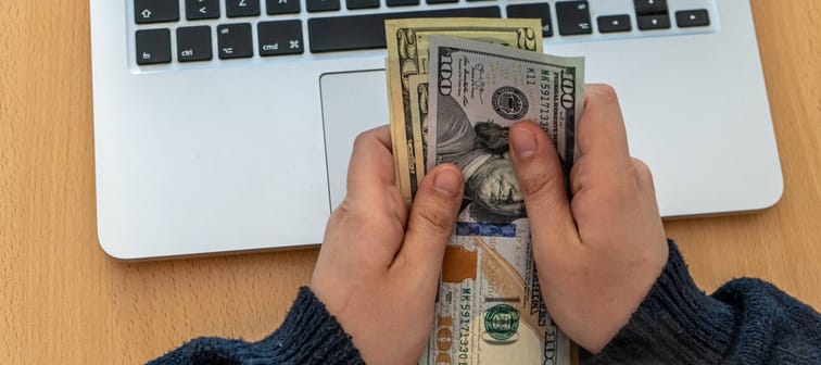 Man holding cash in front of a laptop