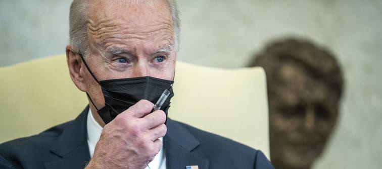 President Joe Biden wearing a mask holding a pen during conversation with staff and media