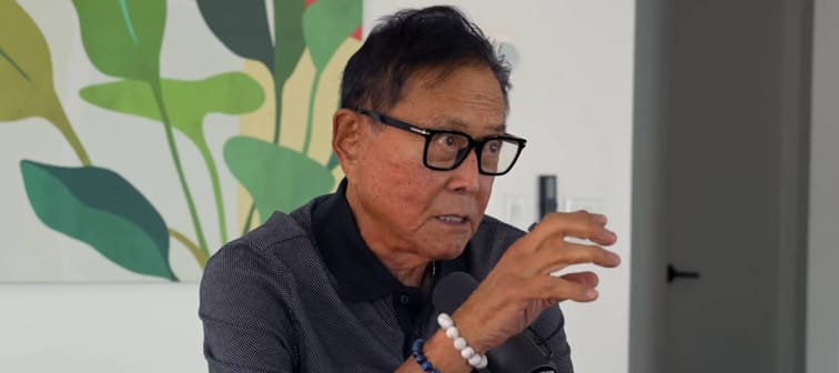 Robert Kiyosaki gestures broadly while speaking into a microphone.