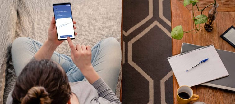 Woman using investment mobile app, shown from above sitting on couch