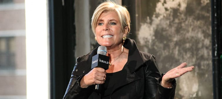 Suze Orman speaks with hand up and microphone held to her mouth