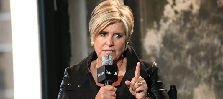 Suze Orman speaks into a microphone with her finger up and pointed