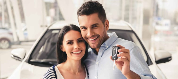 Happy young couple smile at camera, hold keys to new car up to camera