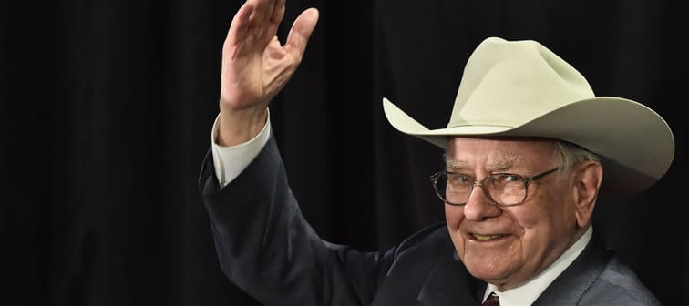 Warren Buffett wears cowboy hat and holds hand up to wave