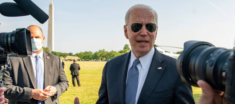 Joe Biden stands outside wearing aviators and talking to a group of reporters.