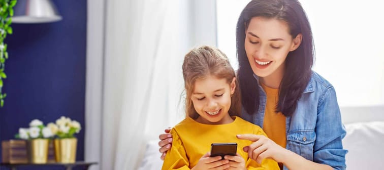 Happy loving family. Young mother and her daughter girl are playing in bedroom. Funny mom and lovely child are having fun with phone.