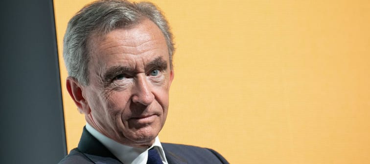 Bernard Arnault makes a cheeky face to the camera in front of a yellow backdrop.