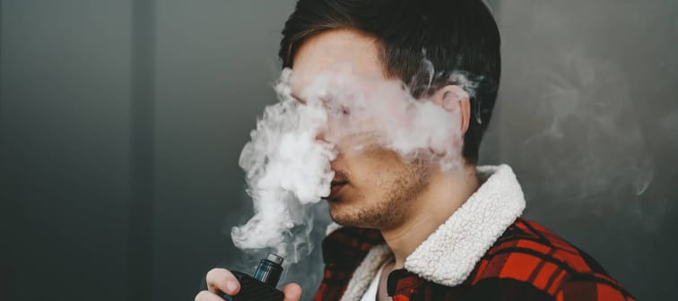 Man wearing a plaid coat uses a vape while surrounded by a cloud of vapors.