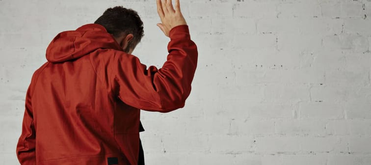 An attractive young man in red jacket waves goodbye shot from the back against white wall background