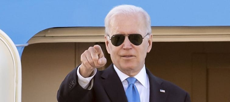 President Joe Biden leaves a plane, wearing sunglasses and pointing his finger.