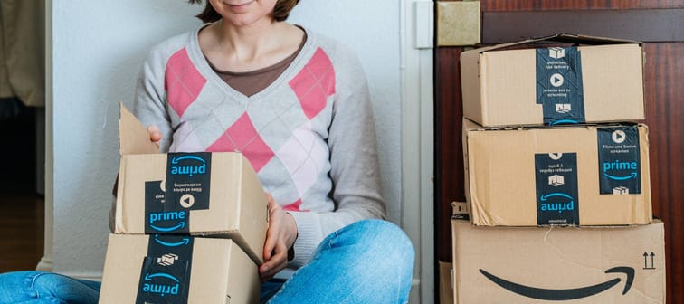 PARIS, FRANCE - JAN 13, 2018: Stack of Amazon Prime packages delivered to a home door smiling woman begin to unbox the cardboard boxes