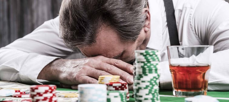 It is not my day. Depressed senior man in shirt and suspenders leaning his head at the poker table with money and gambling chips laying all around him
