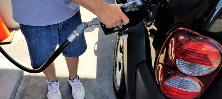 Man stands beside car, filling up gas tank.
