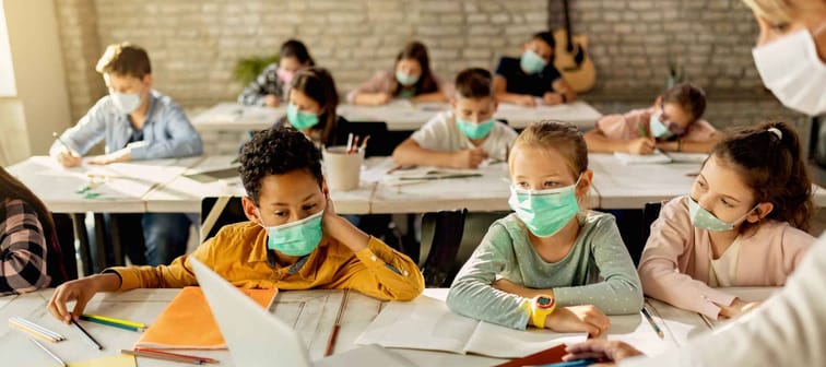 Group of school kids with protective face masks learning on laptop with their teacher during a class in the classroom.