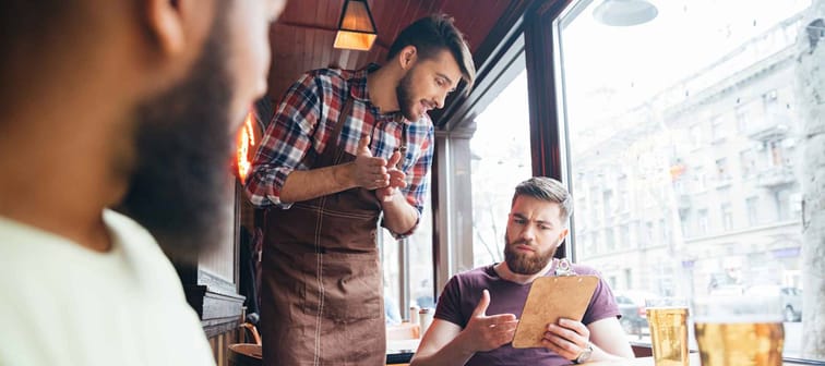 Angry irritated bearded man arguing with waiter about his bill in bar