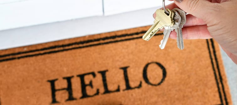 Female hand holding a set of keys over a welcome mat saying Hello - new home