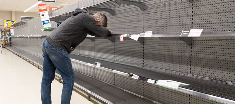 Man stands in supermarket aisle frustrated by empty shelves