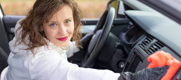 Pretty young woman in a white hoodie makes a wet cleaning in the car with a red rag.