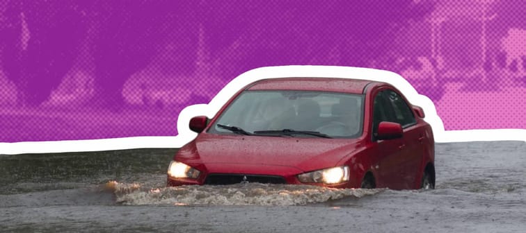 Red car drives through deep flood waters on residential street.