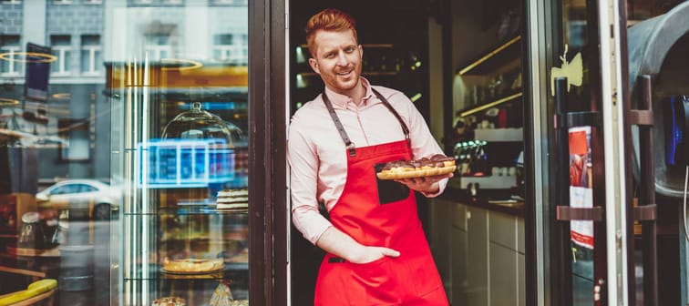 Portrait of happy professional confectioner holding plate with sweet biscuit desserts working at bakery shop
