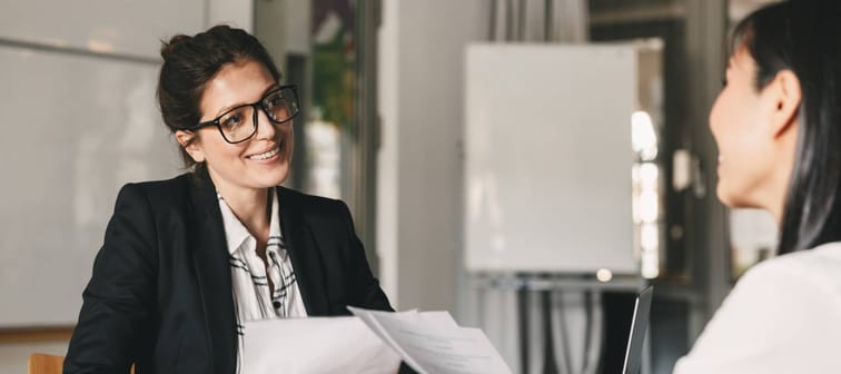 Portrait of smiling businesswoman holding resume and talking to female candidate during corporate meeting or job interview .