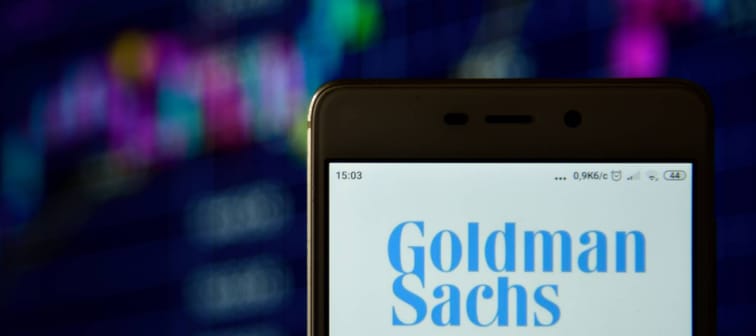 Goldman Sachs logo displayed on a cell phone screen with a stock performance chart in the background
