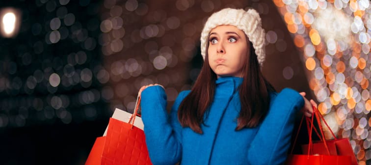 A woman with many holiday shopping bags and her eyes wide takes a deep breath from feeling overwhelmed