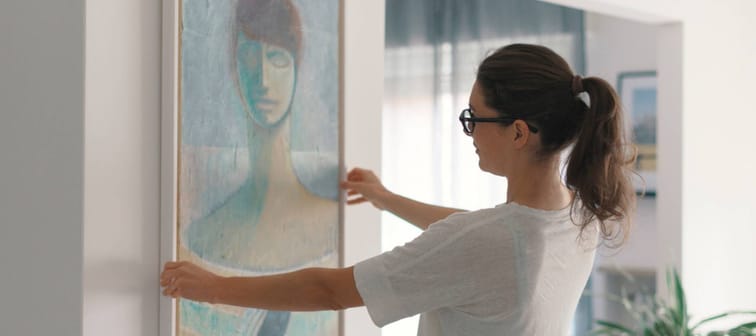 Woman hanging a painting at home and decorating her contemporary living room
