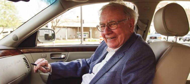 Warren Buffett sits in a car, looking toward camera