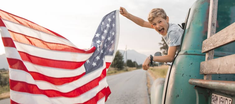 Boy waving American flag out of an old truck
