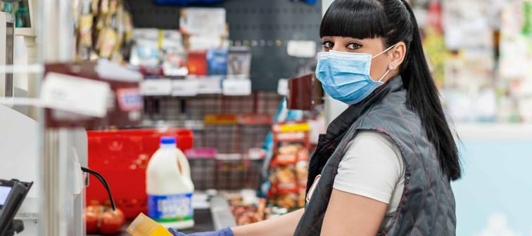 A portrait of young woman in a medical mask and gloves, working at the checkout in a supermarket. Concept of coronovirus, protection from infection and industrial crisis.