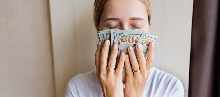 Young Caucasian woman sniffing cash money one hundred dollars bills with closed eyes