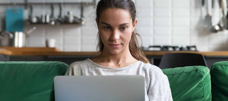 Horizontal photo focused mixed race woman sitting on couch at home working on laptop