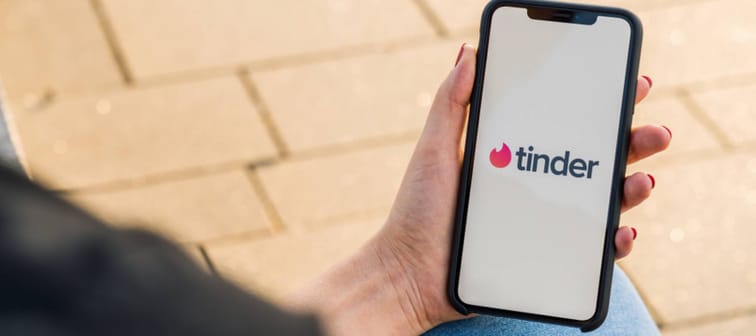 Woman hand holding iphone Xs with logo of Tinder app to log in.