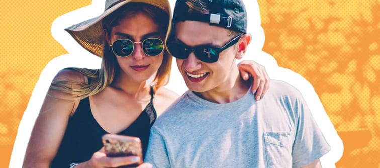 Young couple wearing sunglasses stand looking down at a phone together.