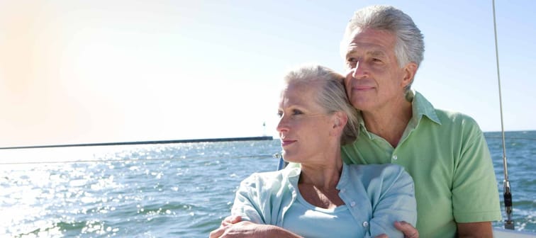Senior couple sitting on the deck of a yacht out at sea and his wife is leaning against him while enjoying the view