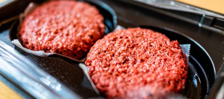 Closeup of two raw uncooked red vegan meat burger patties in plastic packaging