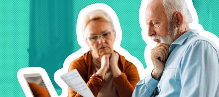 Older couple sit at the kitchen table, looking at documents with looks of concern on their faces.