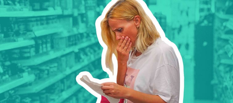 Woman looks shocked at a paper check in a grocery supermarket price increase and inflation.