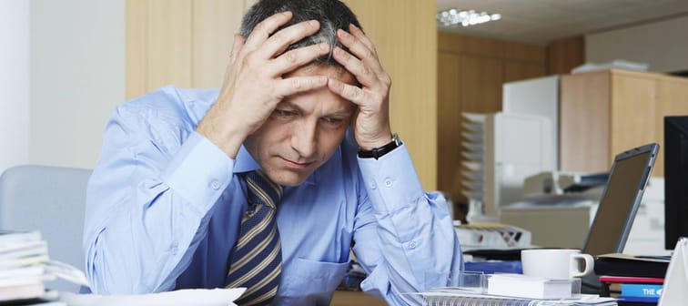 Frustrated middle aged businessman sitting at office desk with his head in his hands.