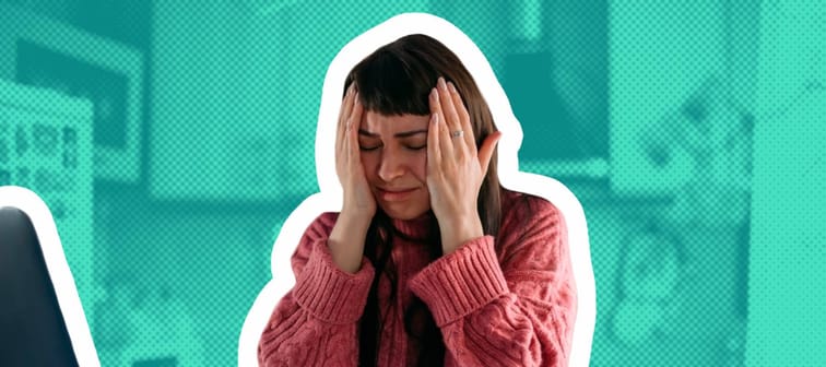 Young woman looks stressed at dining room table, holding her head.