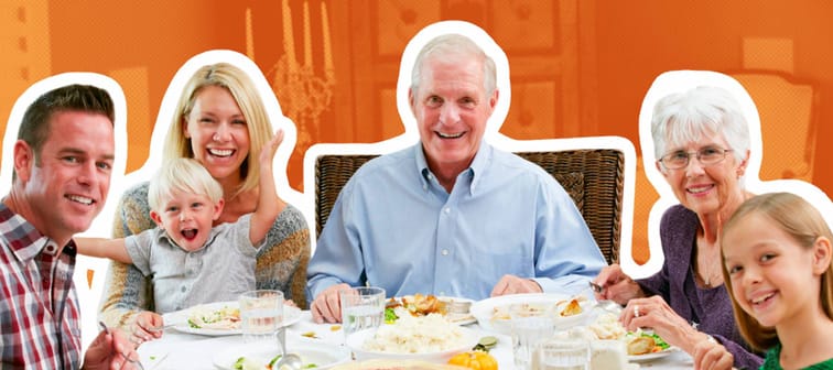 A multi-generational family sits around a table set up with a Thanksgiving feast, smiling for the camera.