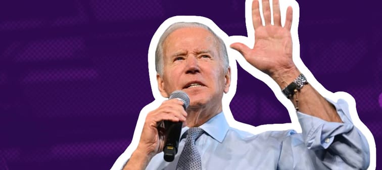 President Joe Biden holds up his hand while speaking into a microphone.